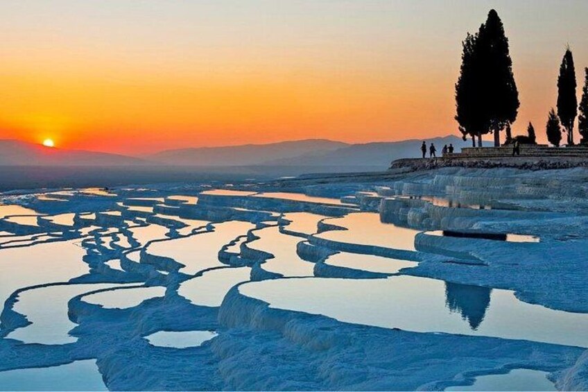 Terraced pools of water, a sunset, and silhouettes of trees and people. 2
