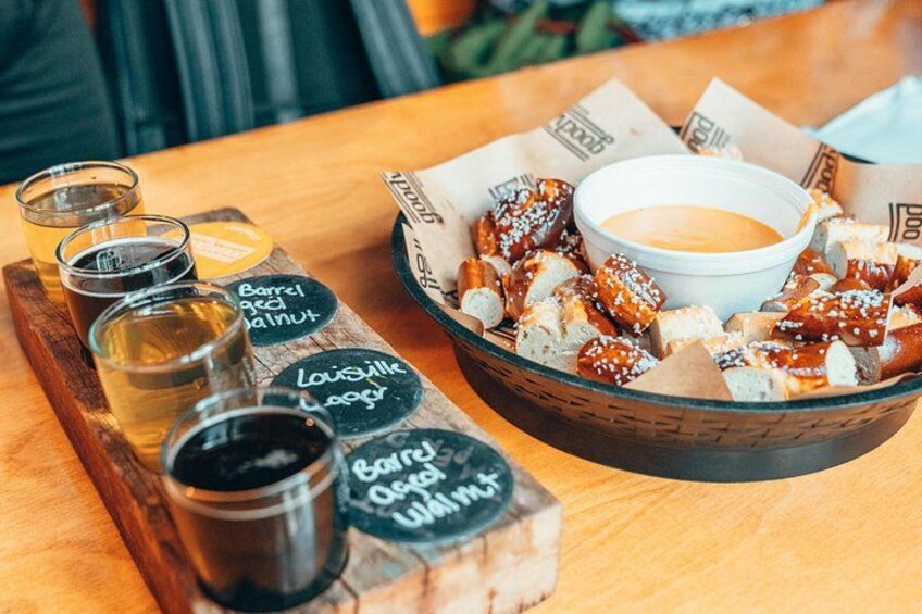 Una bandeja de madera con pretzels y salsa para mojar, un tazón de pretzels y tres vasos pequeños de cerveza. 4
