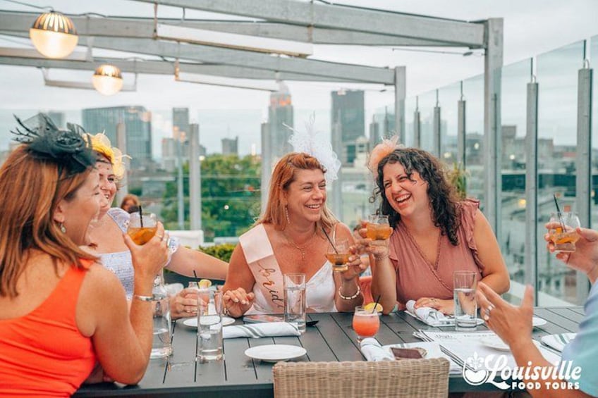 Un grupo de personas brindando en una mesa con bebidas, con vista a un paisaje urbano. 2