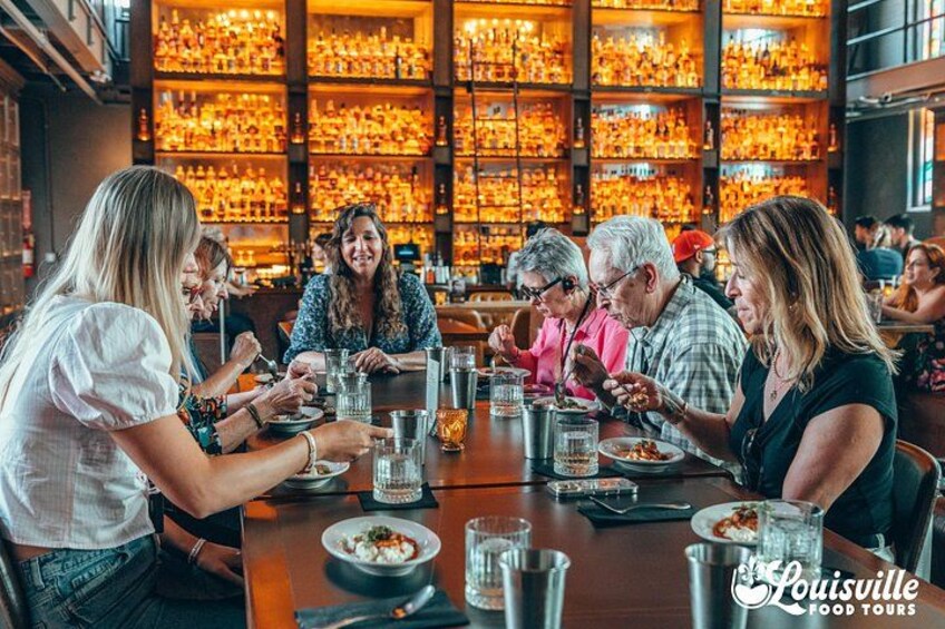 Un grupo de personas cenando en un restaurante con una amplia exhibición de vinos y licores al fondo. 2