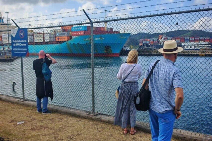 A waterfront with a chain-link fence, a large blue ship, and a sign prohibiting drone use. 2
