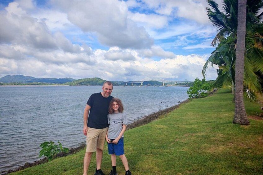 A man and a child standing by a lake with a bridge in the background. 3