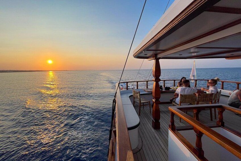 A sunset over the ocean from a boat deck with people seated at tables. 4