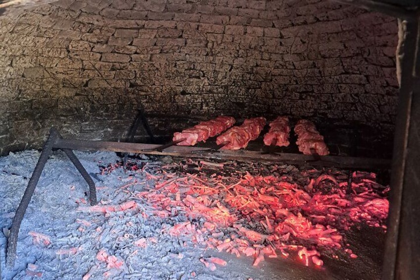 A brick oven with red-hot coals and meat being cooked. 3