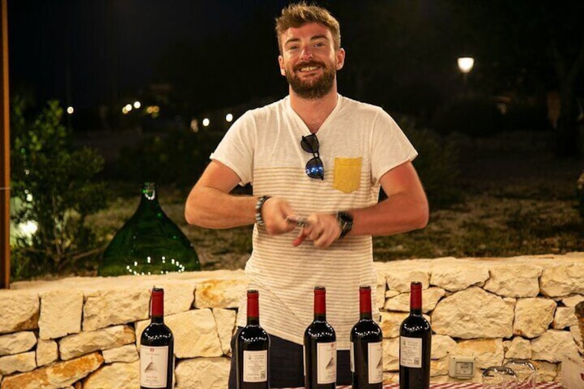 A man standing behind a table with several wine bottles. 3