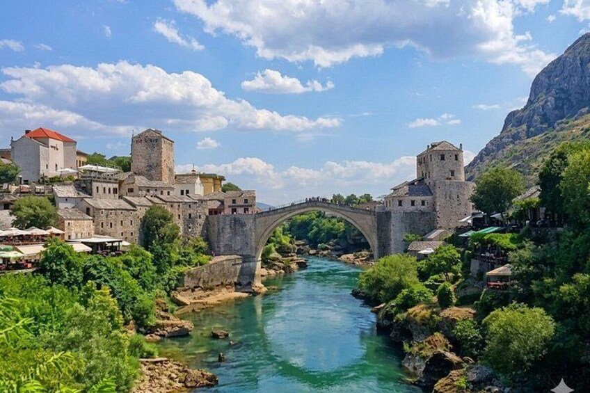 A stone bridge over a river, surrounded by buildings and greenery. 1