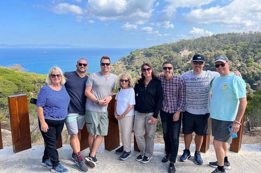 Eine Gruppe von Personen steht auf einer Betonplattform mit einem Panoramablick auf das Meer und Hügel im Hintergrund. 4
