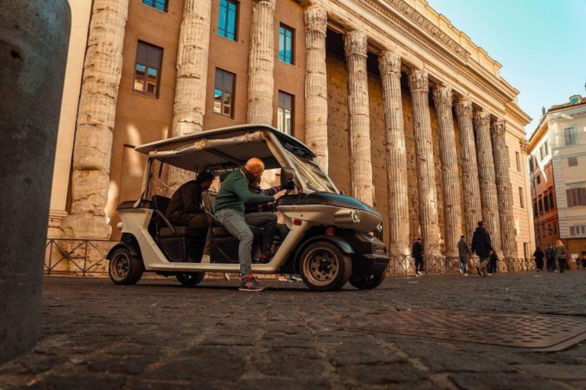 Un carrito de golf con dos personas, un edificio histórico con columnas y adoquines. 5