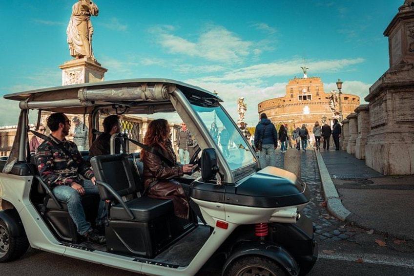 Un carrito de golf con pasajeros en una calle empedrada, una estatua y el Coliseo en Roma. 4