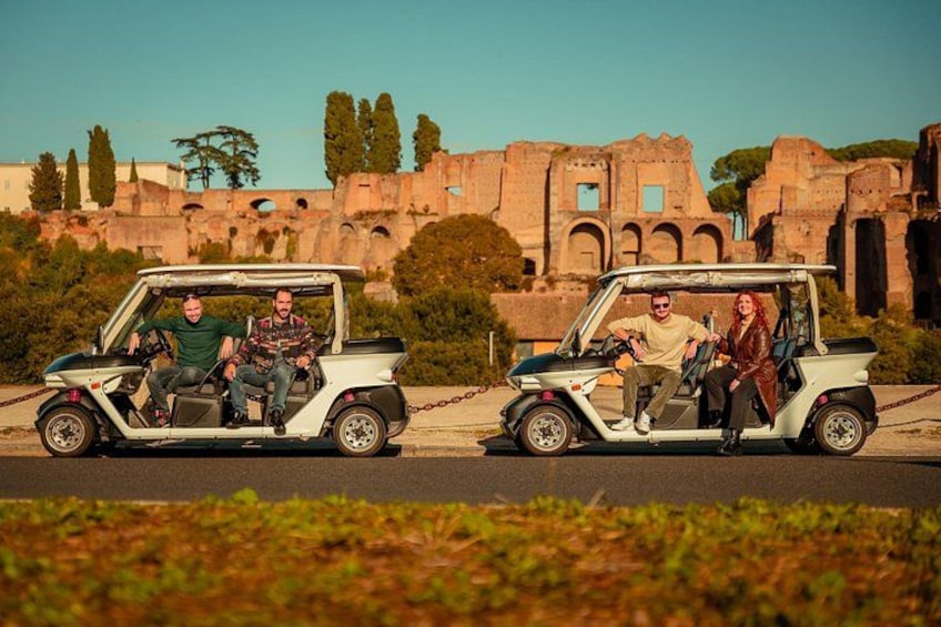Dos carritos de golf con pasajeros, un edificio histórico y árboles al fondo. 3