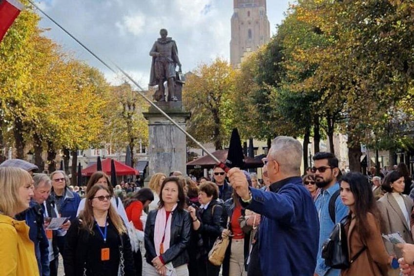 A public square with a statue, people, and a tall building in the background. 2