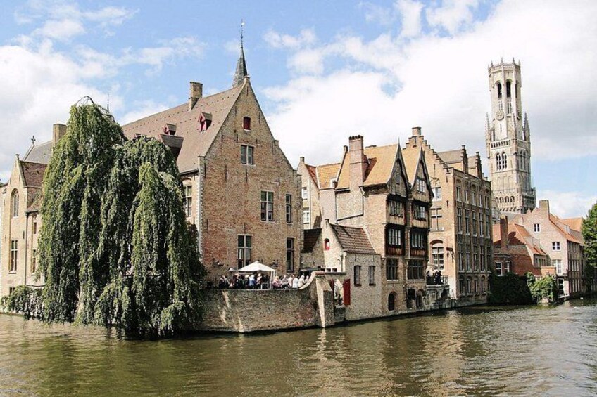 A riverside town with historic buildings, a prominent church tower, and a large weeping willow tree. 1