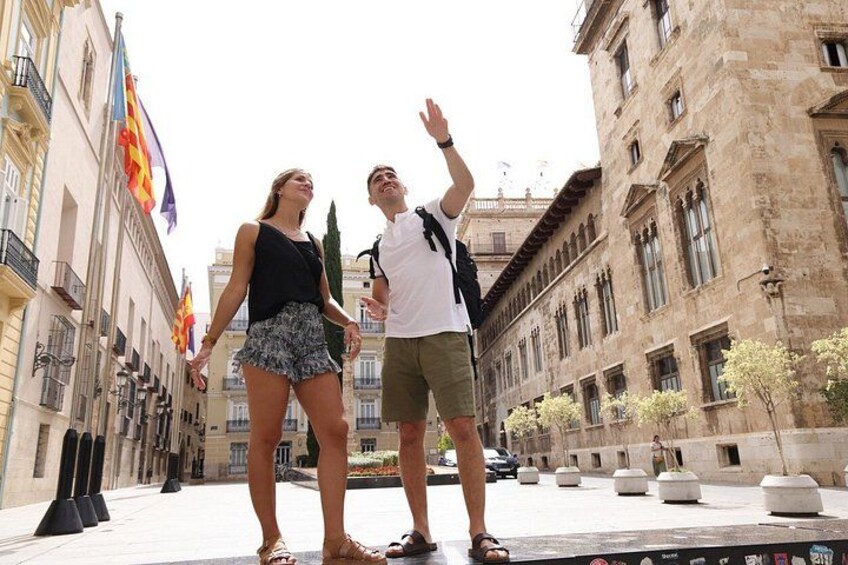 Dos personas caminando por una calle de la ciudad con edificios históricos y banderas. 1