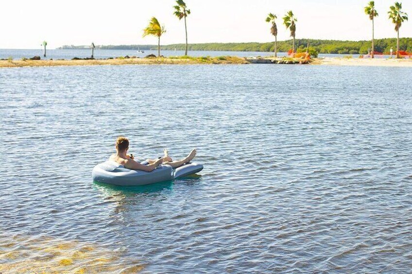 Una persona flota en un tubo acuático en aguas tranquilas, con palmeras y una playa al fondo. 5