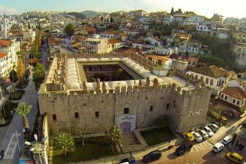 Una fortaleza de piedra histórica con un foso, rodeada de edificios modernos y un cielo despejado. 4