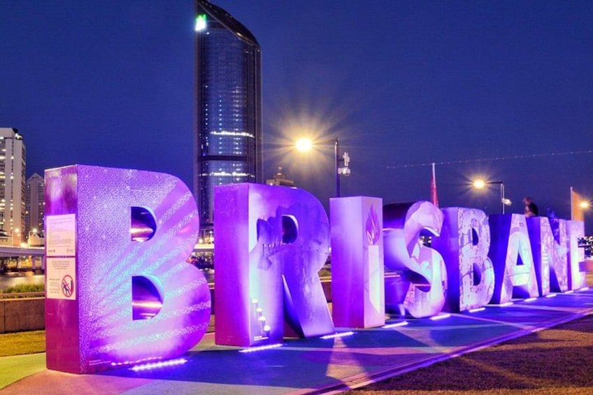 Aufleuchtende Buchstaben, die 'BRISBANE' buchstabieren, mit einem modernen Gebäude im Hintergrund. 3