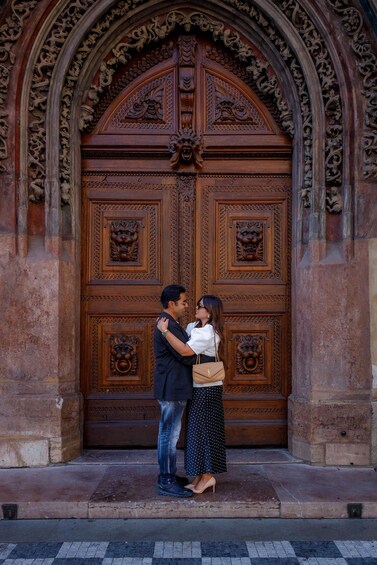 A couple embracing in front of a large, ornate wooden door with intricate carvings. 2