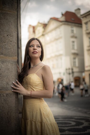 A person in a yellow dress leaning against a stone wall in an urban setting with buildings in the background. 5