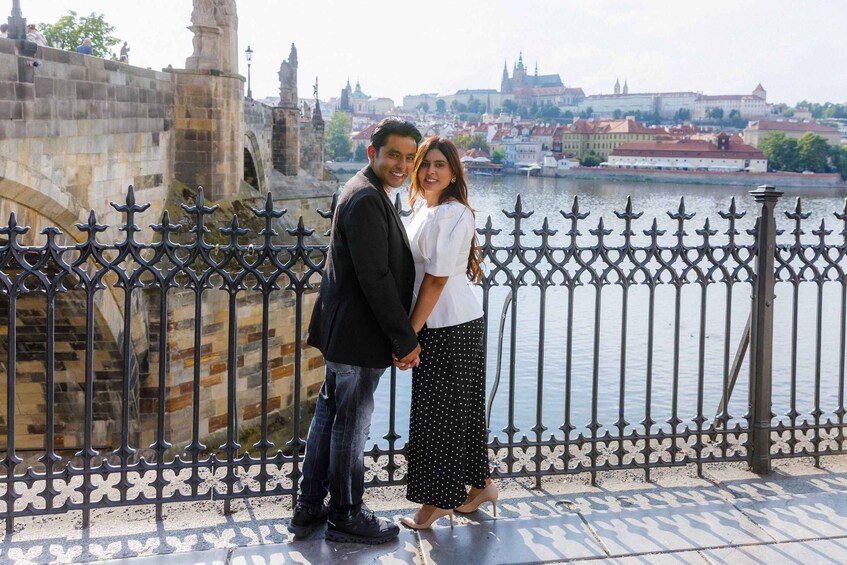A couple standing on a bridge with a river and historic buildings in the background. 3