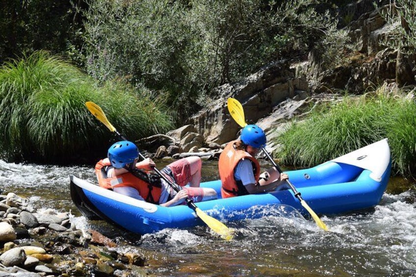 Two people kayaking on a river surrounded by rocks and greenery. 4