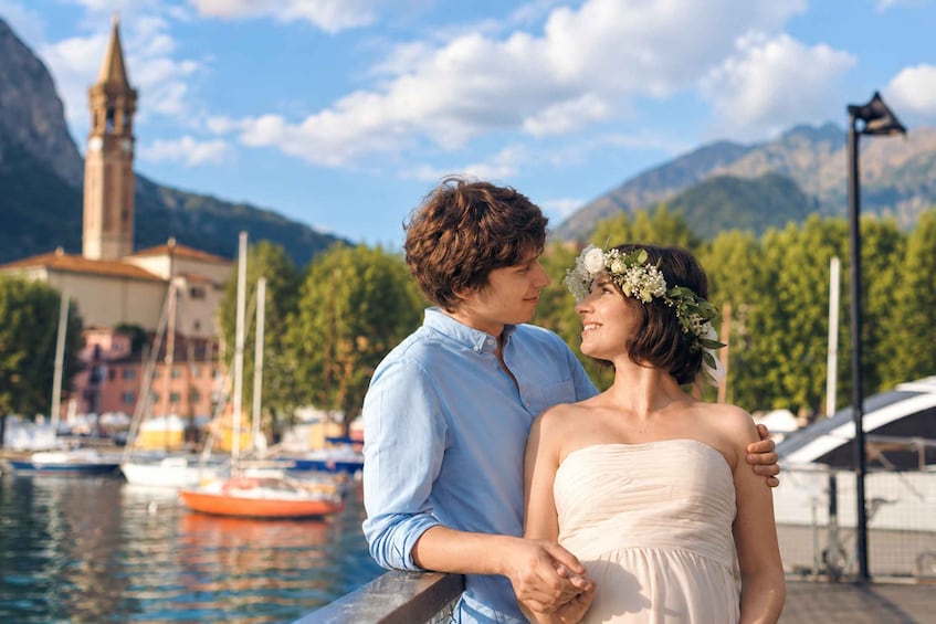 Un couple s’embrasse au bord de l’eau, avec une église et des montagnes en arrière-plan. 1