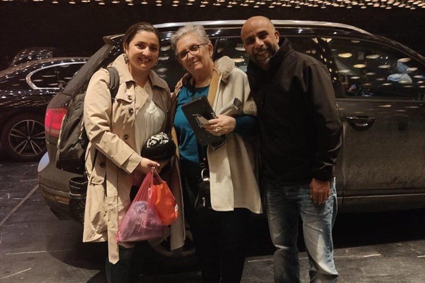 Tres personas de pie frente a un coche con el maletero abierto, un coche negro, y una persona sosteniendo una bolsa negra. 2