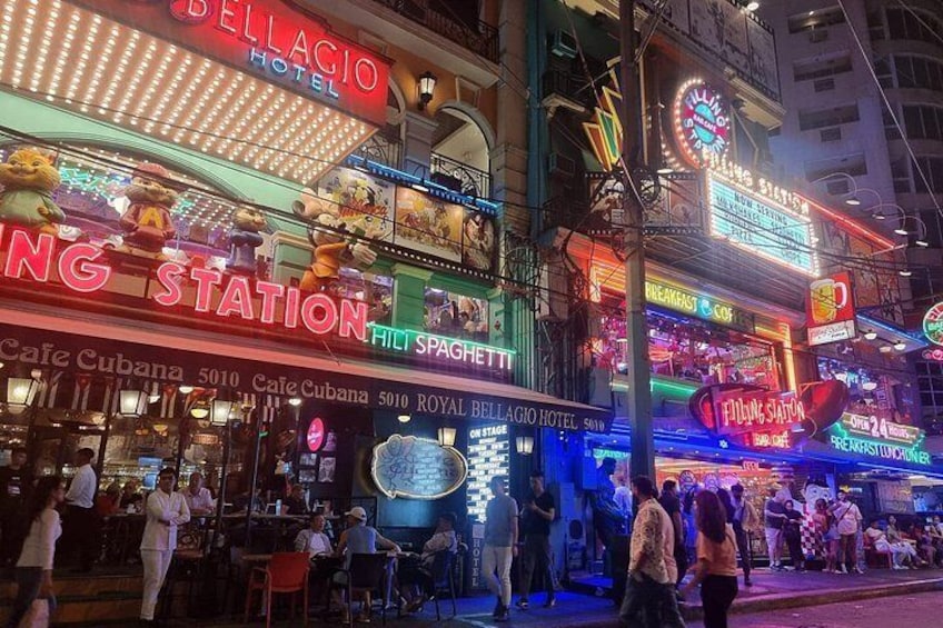 Een straat met felle verlichting en neonreclames, waaronder een hotel en een café. 2
