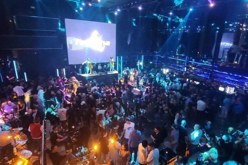 A crowded indoor event with a stage and a large screen displaying an image. 2