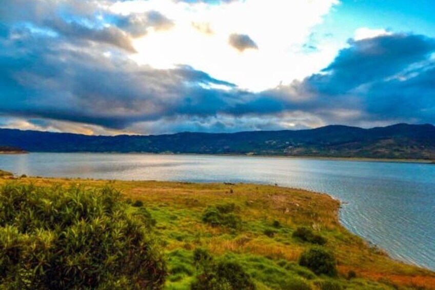 A lake with a grassy shoreline, distant mountains, and a cloudy sky. 3