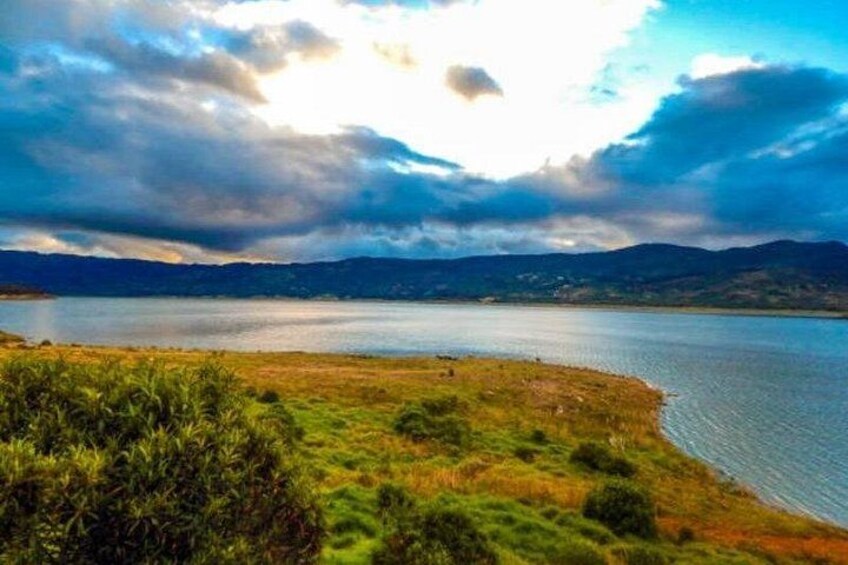 Un lago con orilla cubierta de hierba, montañas distantes y un cielo nublado. 5