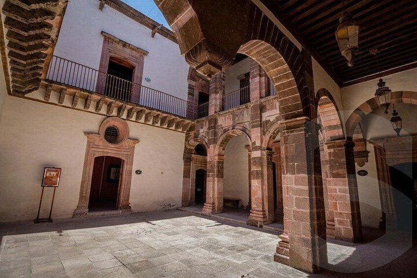 An interior courtyard with arches, a balcony, and a sign. 2