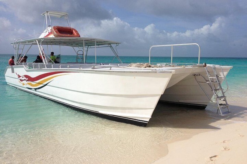 A white boat with a red and yellow stripe, docked on a sandy beach with clear turquoise water. 3