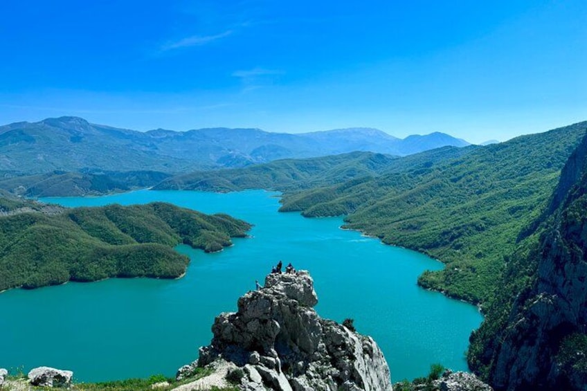 A turquoise lake surrounded by green hills and mountains under a clear sky. 5
