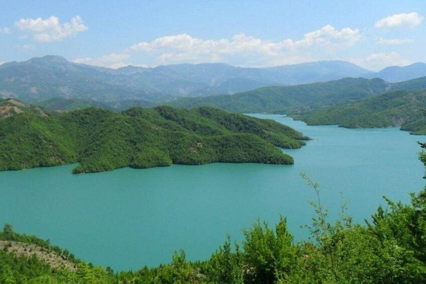 A turquoise lake surrounded by lush green hills and distant mountains under a clear sky. 4