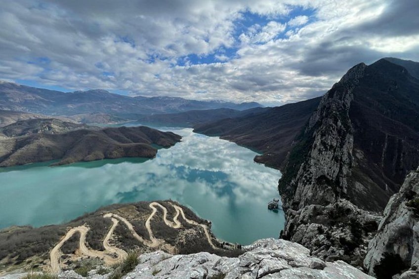 A mountain landscape with a winding path, a turquoise lake, and a rugged peak. 3