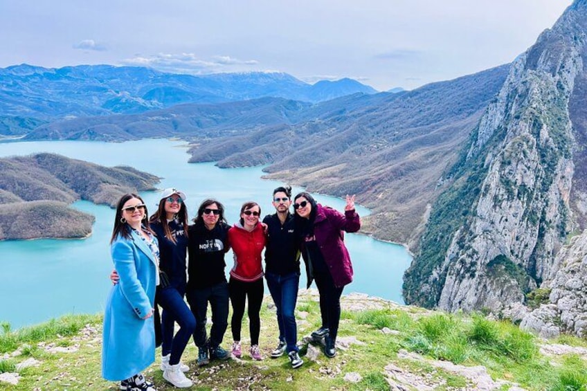 A group of people standing on a mountain edge with a lake and mountains in the background. 5