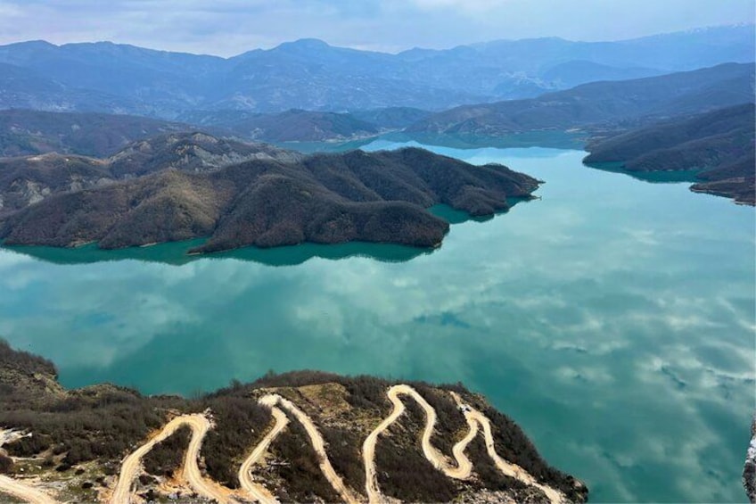 A mountainous landscape with winding roads and a large turquoise lake. 4