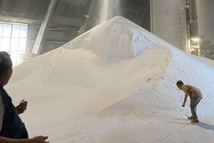 A large pile of snow in an industrial setting with a person standing on the snow. 2