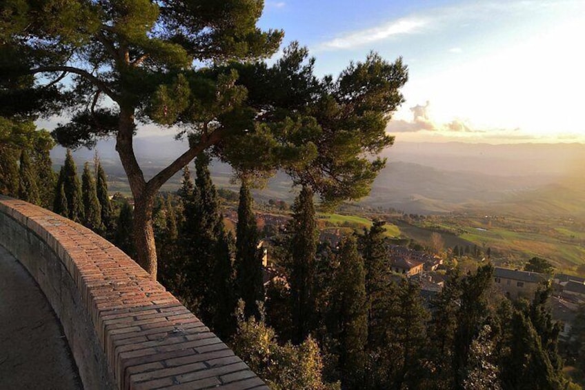 A landscape with a brick wall, tall trees, and a distant view of a town. 4