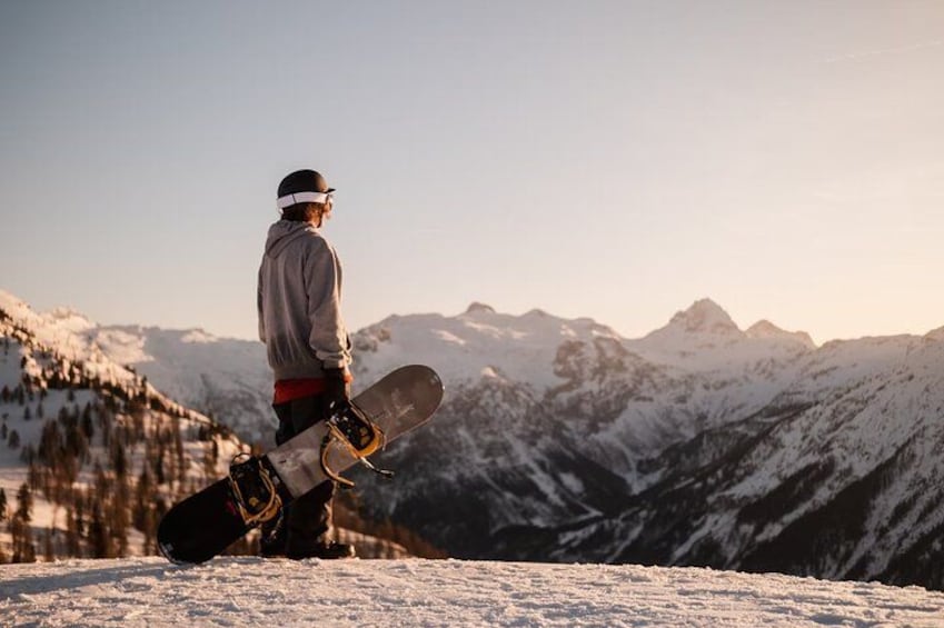 A person standing on a snowy mountain holding a snowboard, with snow-covered mountains in the background. 4