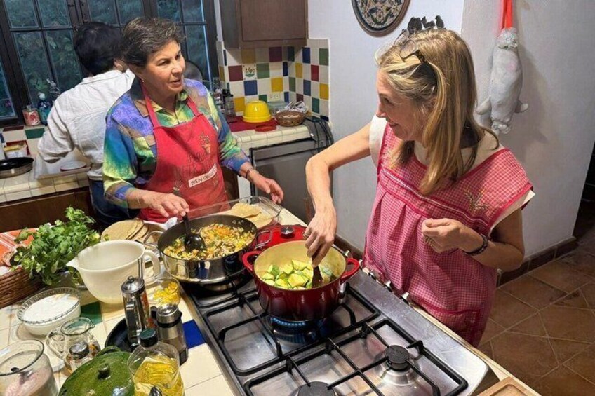 A kitchen with people cooking, a stove, pots, and a window. 2