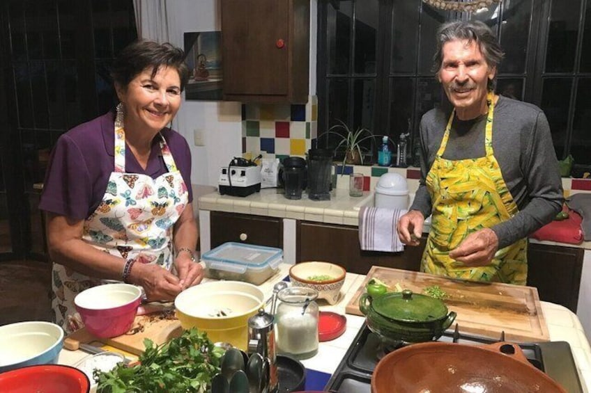 Two people in a kitchen with various cooking utensils and ingredients on the counter. 1