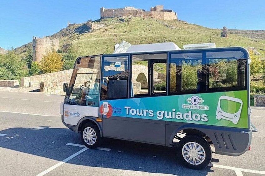 A green and white bus with 'Tours guiados' and 'Eco City Tour' on the side, parked on a road with a castle in the background. 5