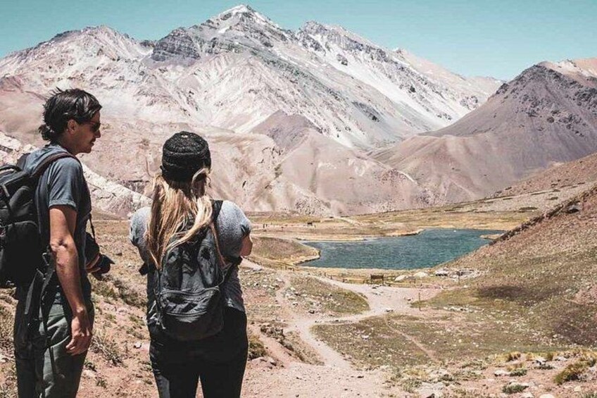 Two hikers on a mountain trail with a lake and mountains in the background. 1