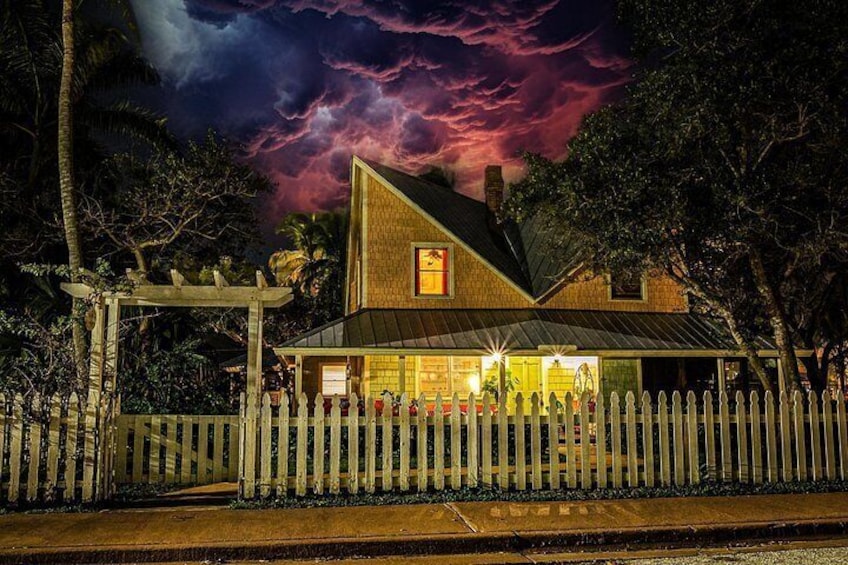 A house with a white picket fence, a porch, and a dark sky with clouds. 4