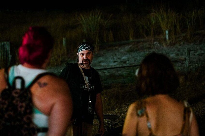 A person in a black t-shirt with a bandana, standing outdoors at night. 5