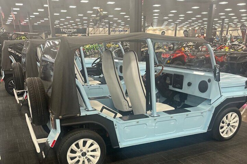 A light blue off-road vehicle with a black roof and beige seats, displayed in a showroom with other vehicles. 3