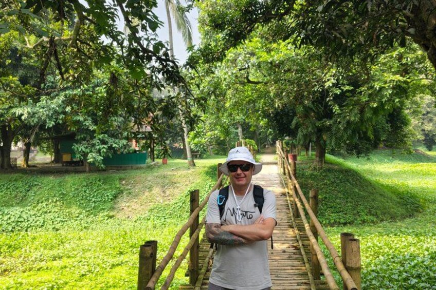 A person standing on a wooden bridge in a lush green park with trees and a pathway. 5