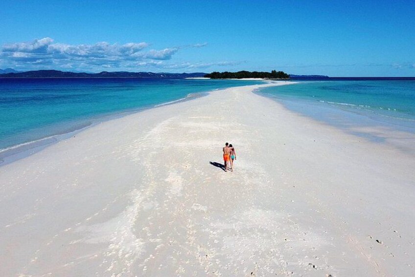A beach with clear turquoise water and a person walking towards the water. 1