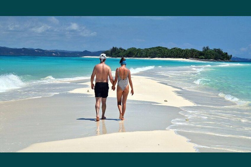 A couple walking on a beach with clear turquoise water and a distant island. 4